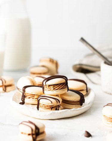 Stacked macarons on a while plate surrounded by a milk jug and chocolate chips.